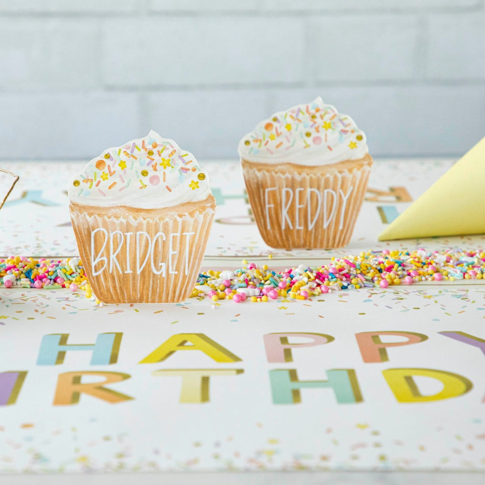 A life-sized Hester &amp; Cook Cupcake Place Card sits atop a party place setting accessory, surrounded by confetti and a birthday banner.