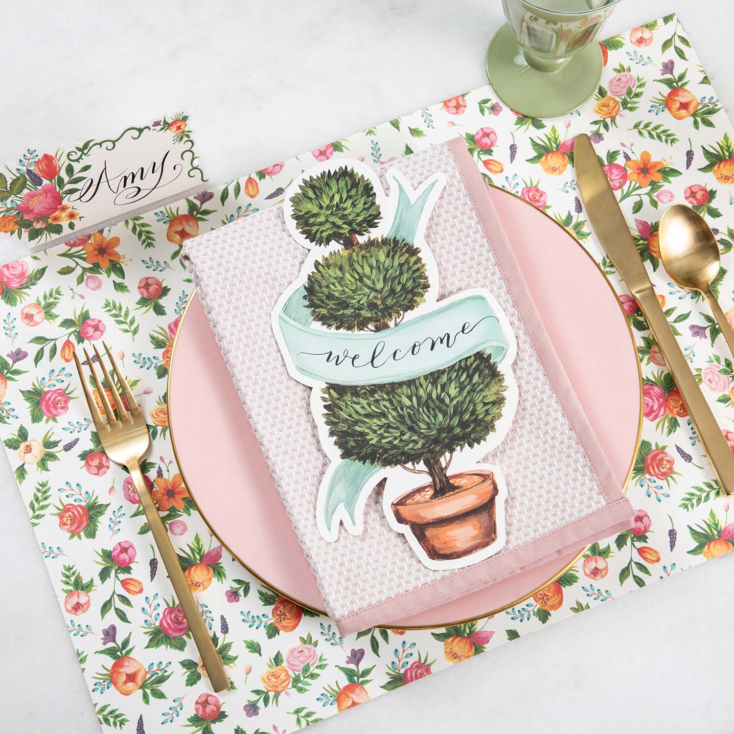 An elegant place setting featuring a Topiary Table Accent with &quot;Welcome&quot; written on the ribbon resting on the plate.