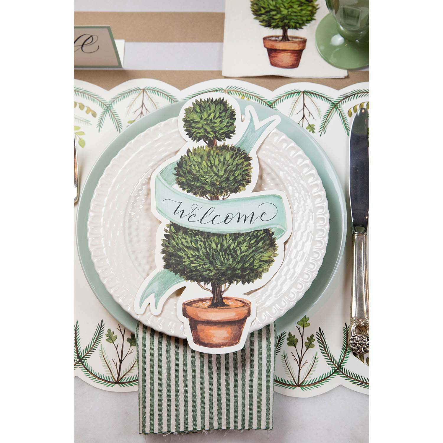 An elegant place setting featuring a Topiary Table Accent with &quot;Welcome&quot; written on the ribbon resting on the plate.