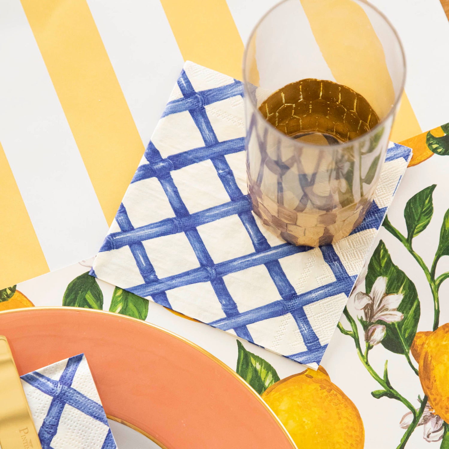 A place setting with a Blue Lattice Cocktail Napkin under a gold-accented glass.