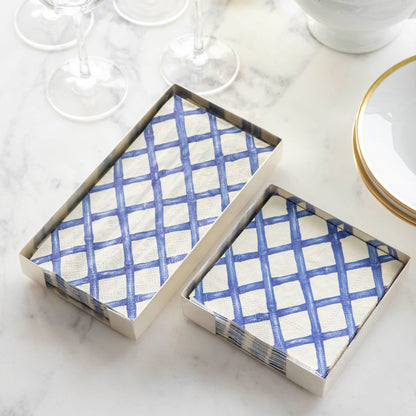 A stack of Blue Lattice Guest Napkins and a stack of Blue Lattice Cocktail Napkins in silver napkin holders on a marble table.