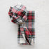 A crumpled Taylor Linen Aberdeen Plaid Napkin lying on a white surface.