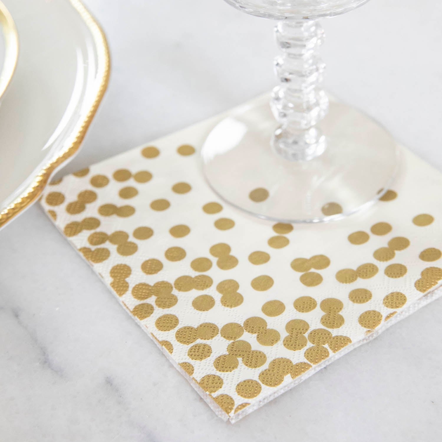 A Gold Confetti Cocktail Napkin under a water glass in an elegant place setting.