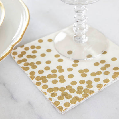 A Gold Confetti Cocktail Napkin under a water glass in an elegant place setting.