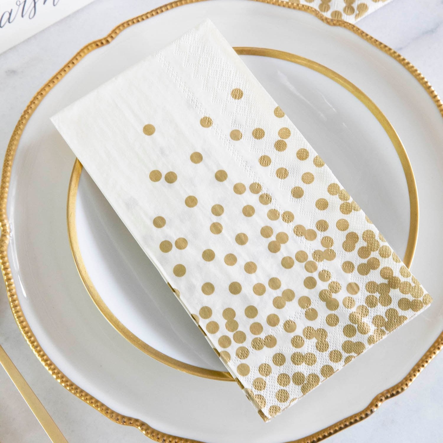 An elegant place setting featuring a Gold Confetti Guest Napkin on the plate, and a Gold Confetti Cocktail Napkin under the glass.