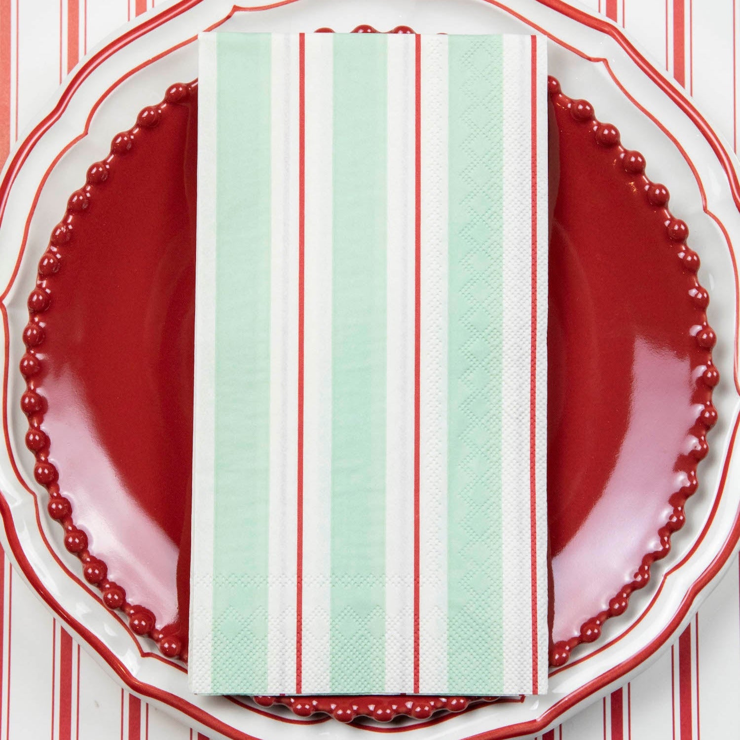A Seafoam &amp; Red Awning Stripe Guest Napkin centered on the plate of a place setting.
