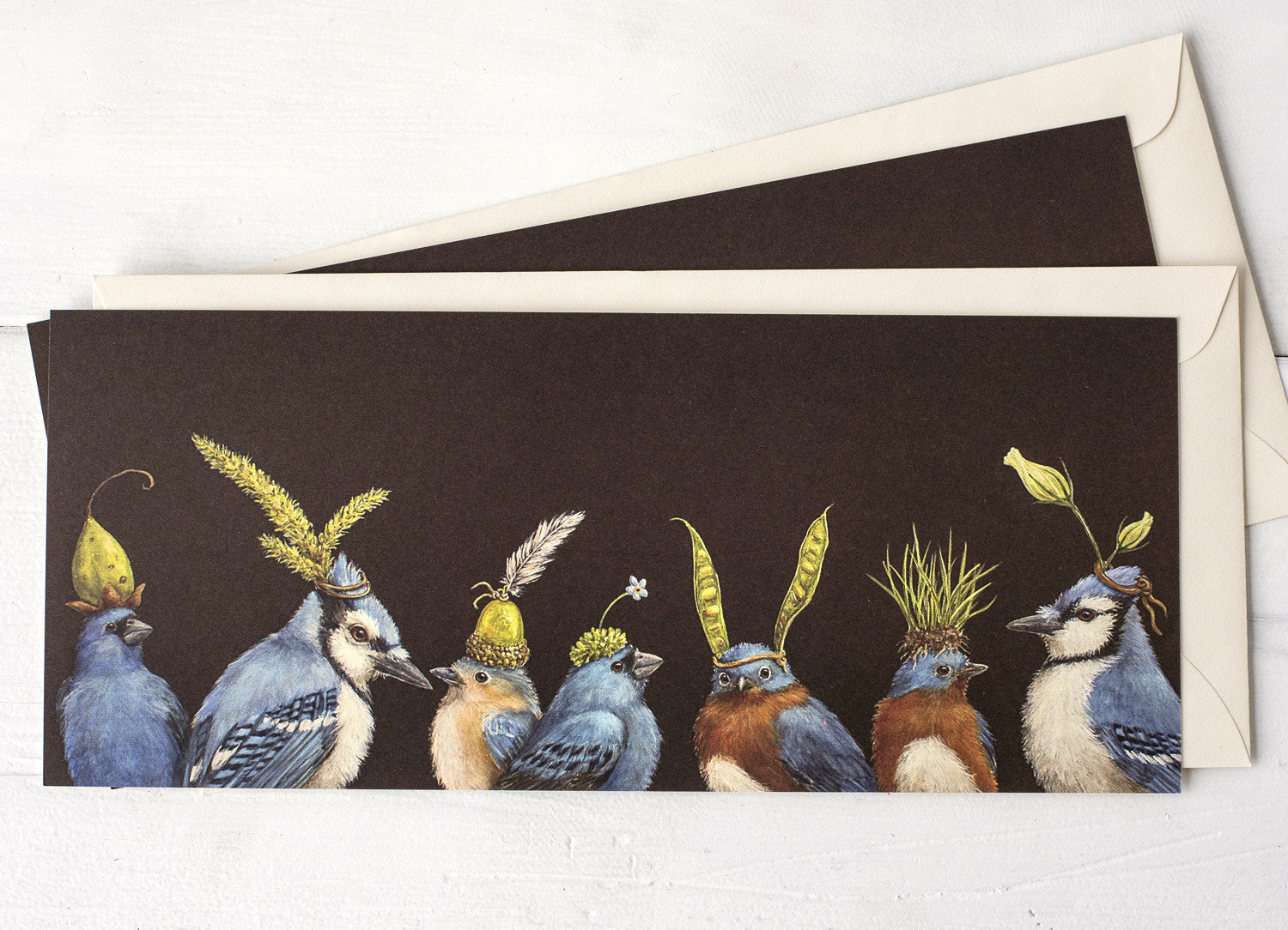 A dark brown greeting card featuring a row of blue songbirds wearing flowers and botanicals as hats, with the included envelope tucked behind the card. 