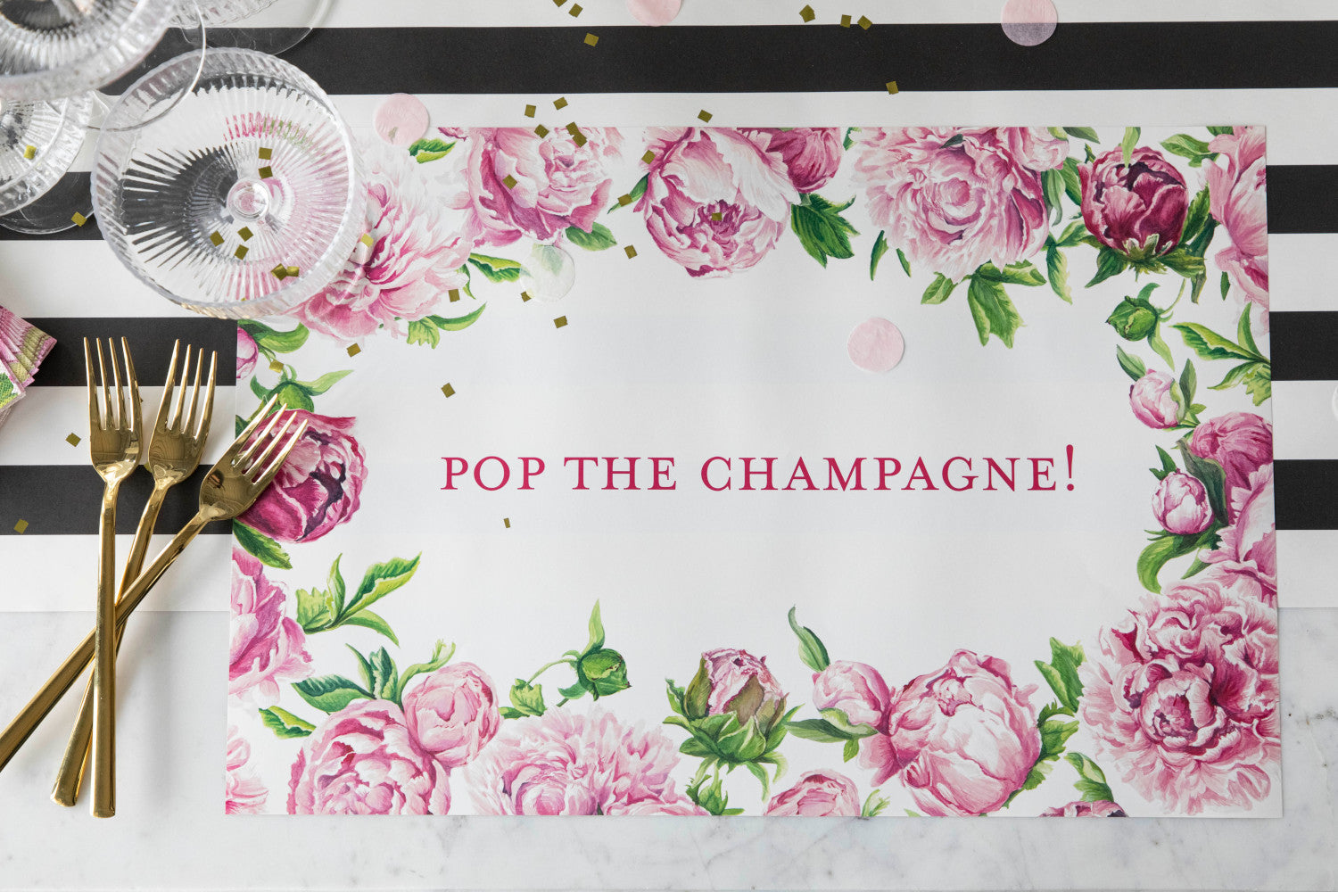 The Peony Personalized Placemat under a festive place setting, with &quot;POP THE CHAMPAGNE!&quot; printed in deep pink, from above.