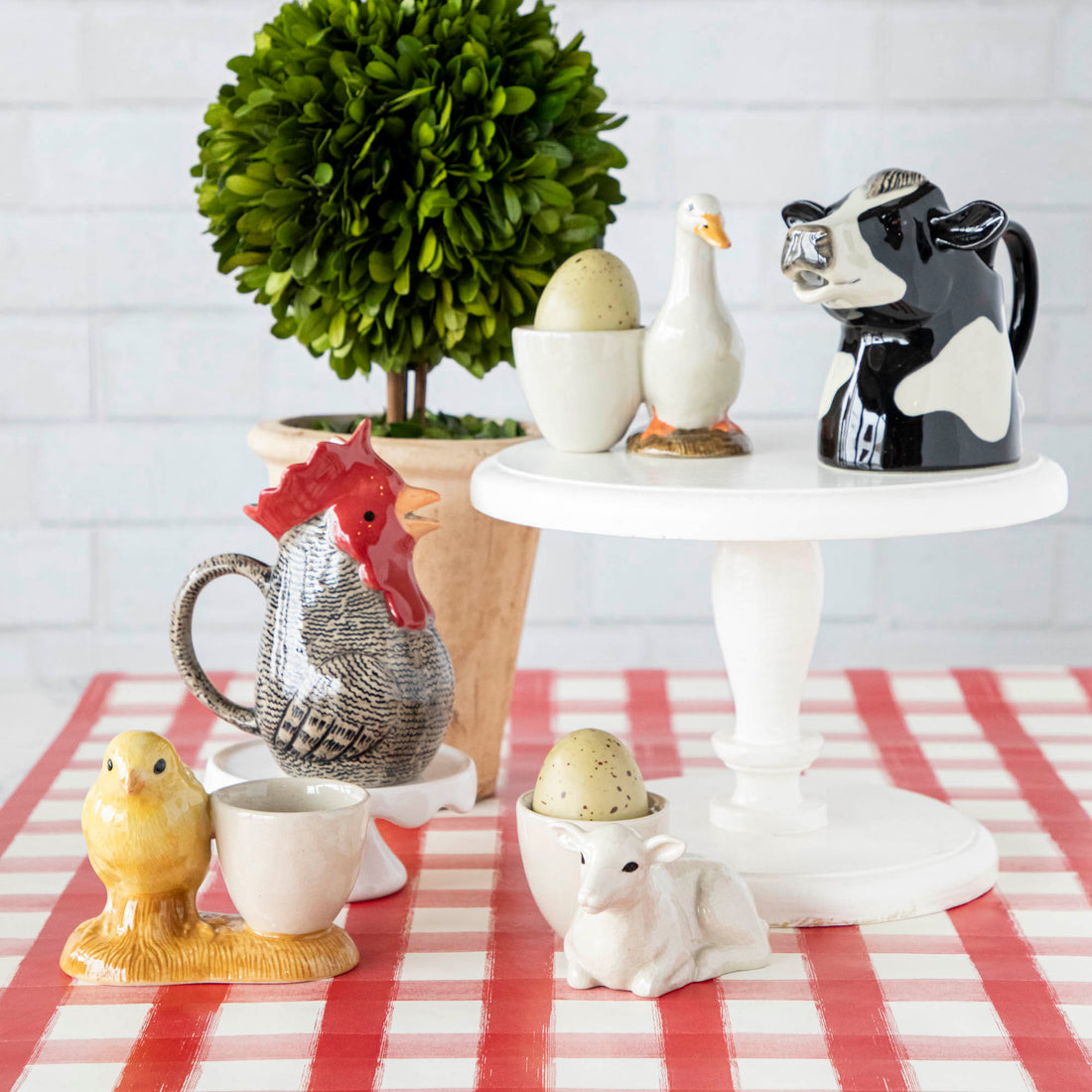 A red and white checkered tablecloth adorned with quirky Farm Animal Ceramics from the British brand, Quail.