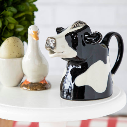 A quirky Farm Animal Ceramics cow jug from the Quail brand sits on a table.