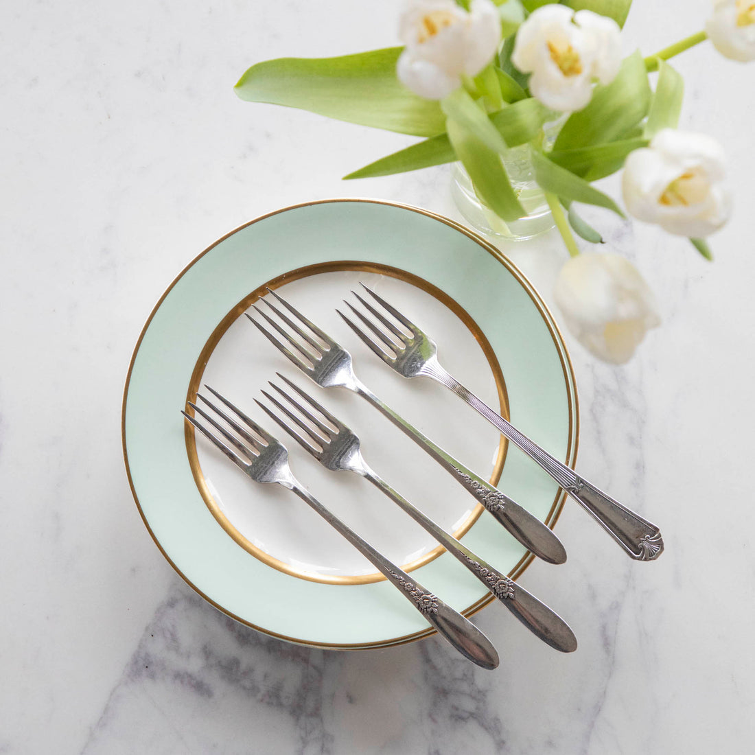 Elegant table setting with mint green plates, Hester &amp; Cook vintage silver-plate long handled salad fork set of four, and white tulips on a marble surface.