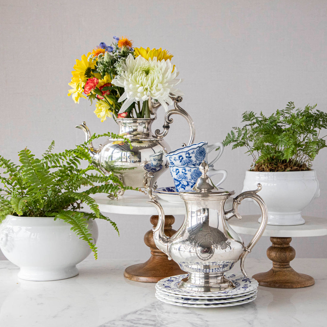 A blue and white table setting with a vase of tulips and Hester &amp; Cook vintage silver-plated tea servers.
