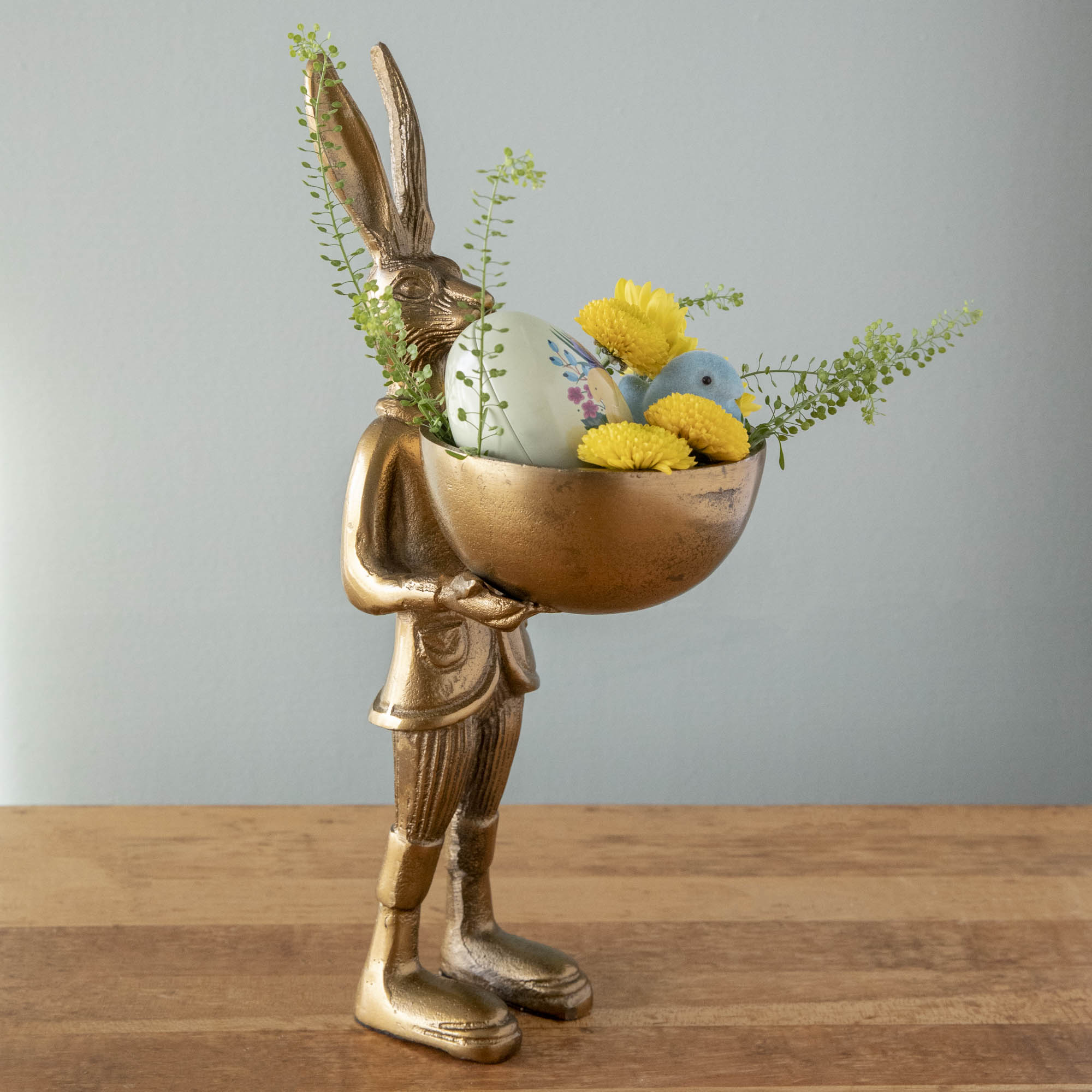 A well-dressed Hare Dish Stand by Accent Decor holding a round dish filled with a decorative egg, flocked chick and flowers. 