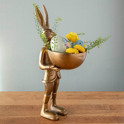 A well-dressed Hare Dish Stand by Accent Decor holding a round dish filled with a decorative egg, flocked chick and flowers. 