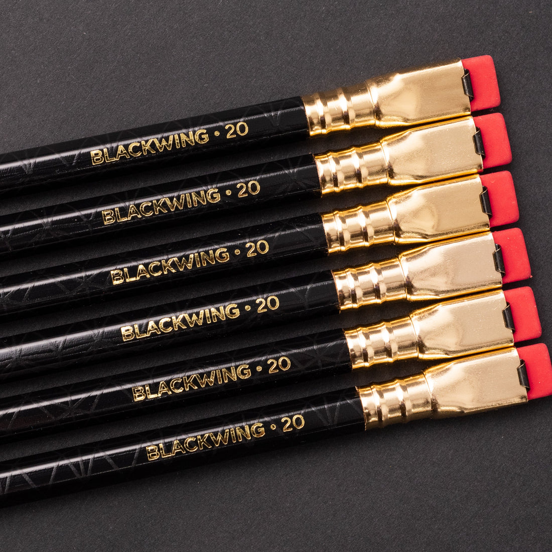 A stack of Blackwing Volume 20- Tribute to Tabletop Games pencils with gold lettering and distinctive square erasers on a black background.