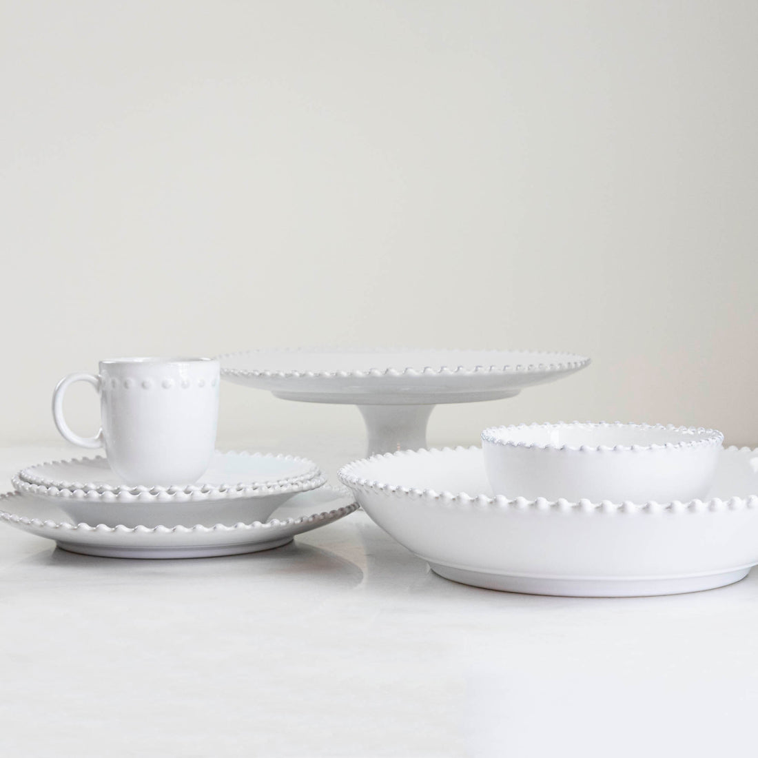 A set of Costa Nova Pearl White Dinnerware with beaded edge design displayed against a light background.