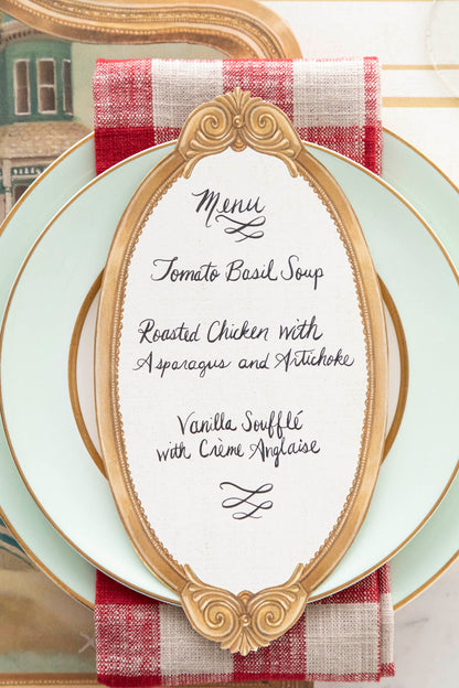 An Antique Gold Frame Table Card with a menu written on it in lovely cursive resting on the pate of an elegant place setting.