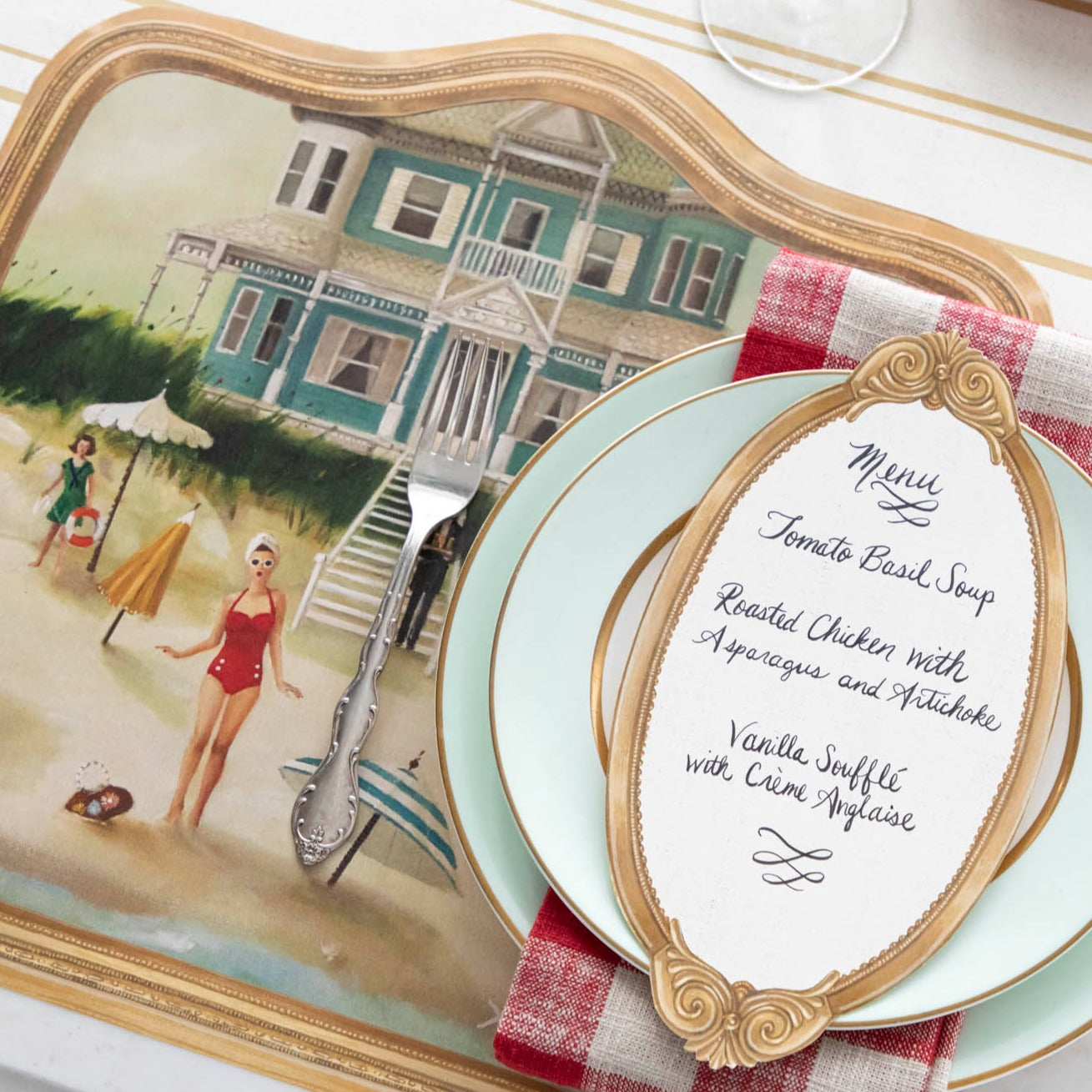 An Antique Gold Frame Table Card with a menu written on it in lovely cursive resting on the pate of an elegant place setting.