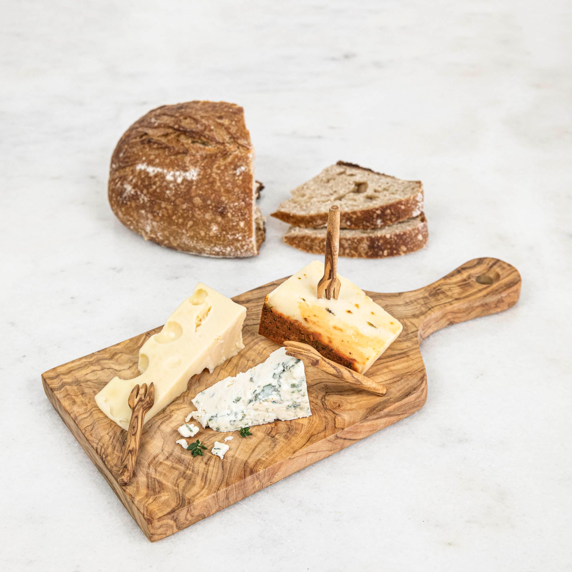 A set of Mini Olive Wood Appetizer Forks (Set of Four) from Natural Olivewood beside a piece of cheese on a wooden cutting board, ready for hors d&