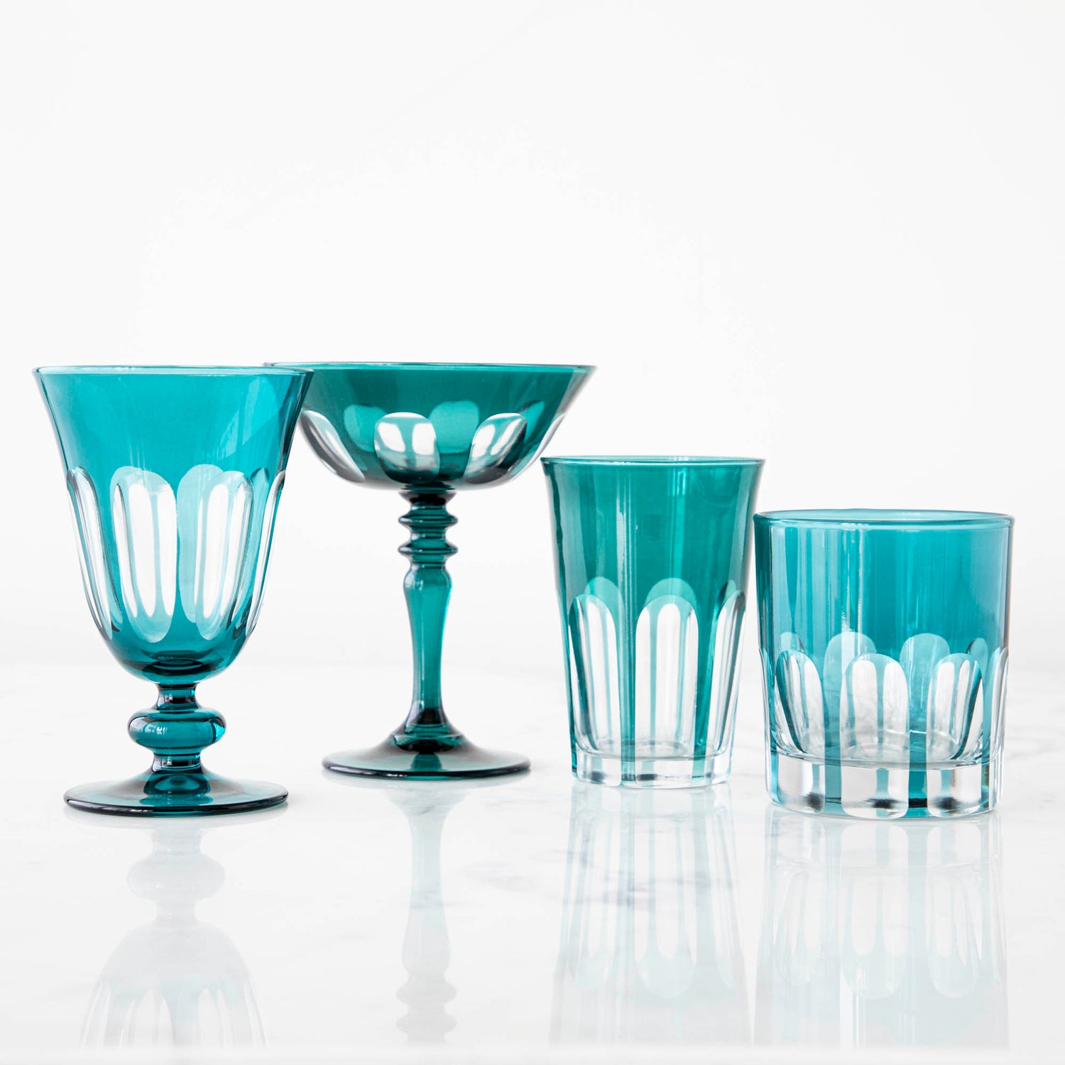 Set of four bespoke Rialto Millicent (Dark Green) glasses by SIR/MADAM on a reflective surface against a white background.