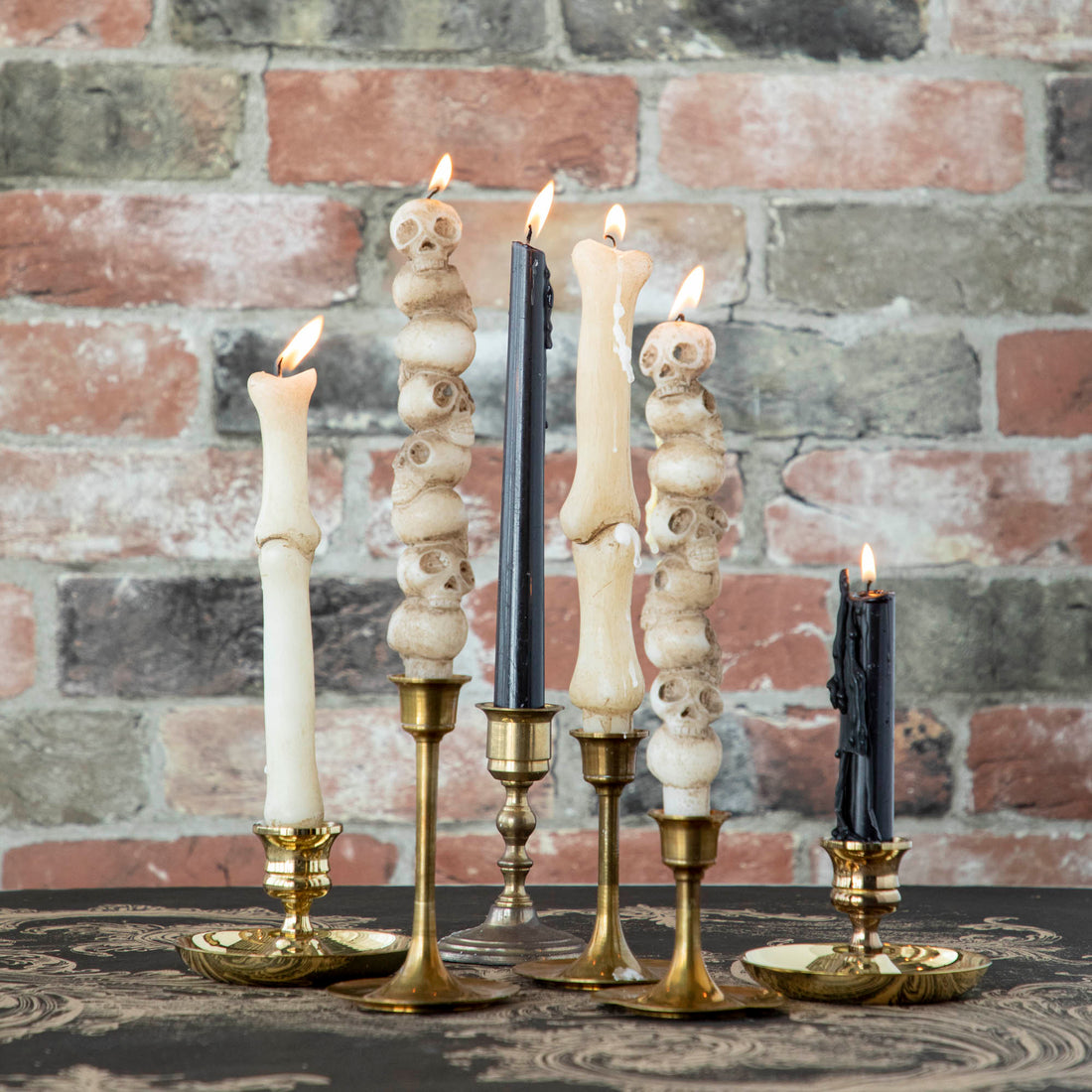 An assortment of taper candles in black, stacked skulls, and bone shaped in brass candlestick holders.  