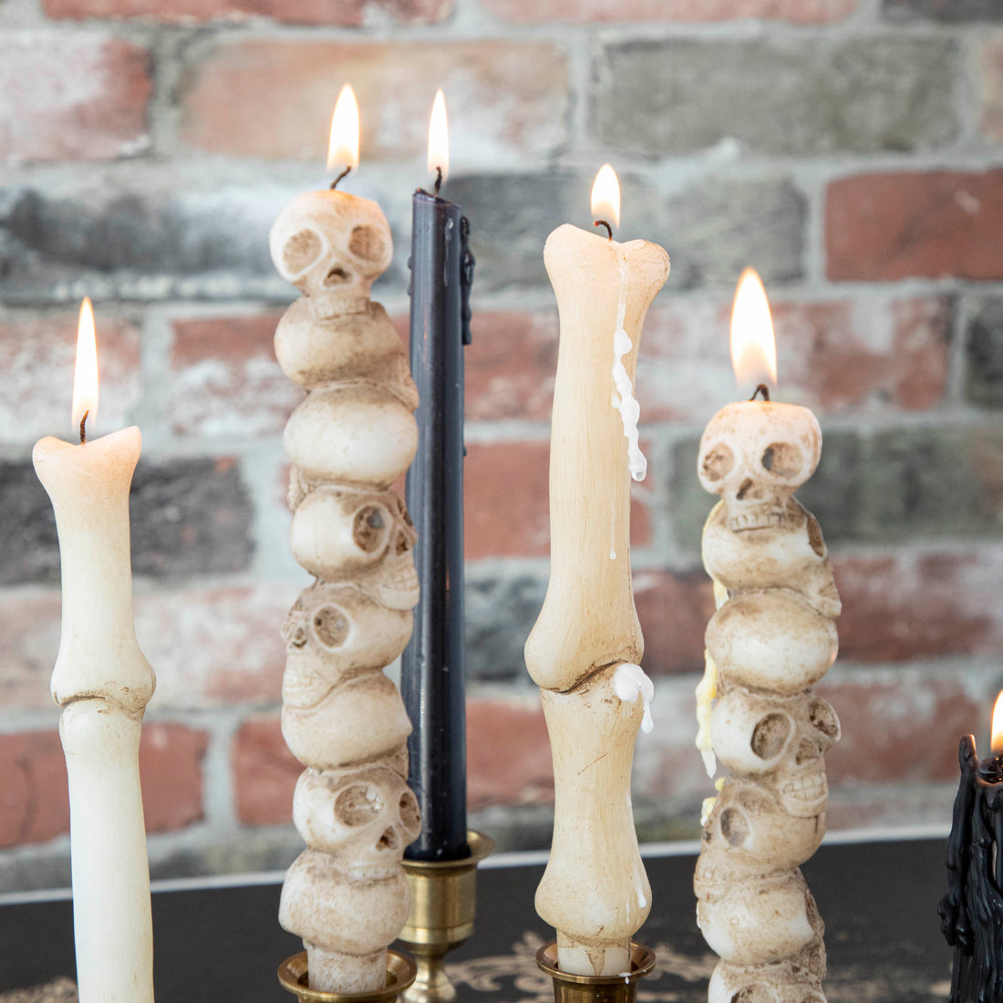 An assortment of taper candles in black, stacked skulls, and bone shaped in brass candlestick holders.  